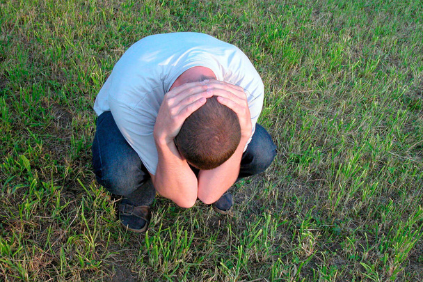 homem agacha-se em um prado verde com as mãos no pescoço, símbolo de depressão, saúde mental
 - Foto, Imagem