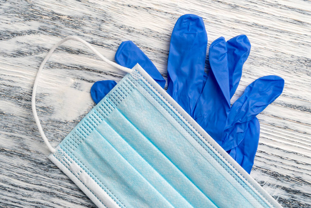 Медицинская защитная маска и нитриловые голубые перчатки на деревянном фоне. Защитный набор для гигиены. Коронавирусная дезинфекция - Фото, изображение
