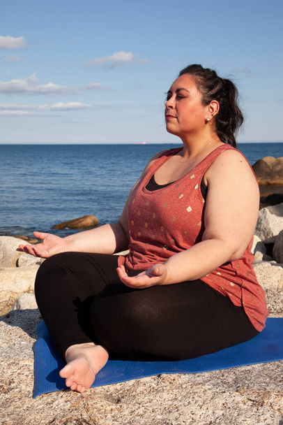 békés nő meghívja spiritualitás vagy éberség, miközben ül a sziklás tengerparton  - Fotó, kép