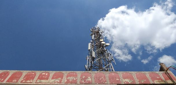 Снимок телефонной башни с облаками в голубом небе, выглядящими как дым, выходящий из дымохода. - Фото, изображение