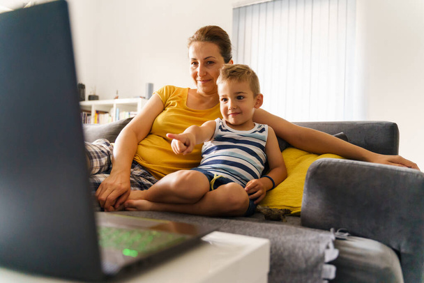 Μικρό καυκάσιο αγόρι δείχνει με το δάχτυλο την οθόνη σπρώχνοντας τη μητέρα του, ενώ βλέποντας online περιεχόμενο στο laptop - Μικρό παιδί γιος κάθεται δίπλα στη μαμά του στο σπίτι μπροστά από τον υπολογιστή - έννοια της παιδικής ηλικίας - Φωτογραφία, εικόνα