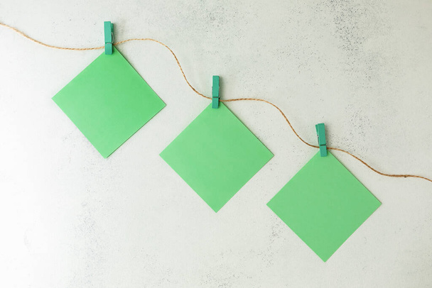 Zelené listy papíru visí na barevných dřevěných kolících na provaze, na bílém, otlučeném pozadí. Plocha - Fotografie, Obrázek