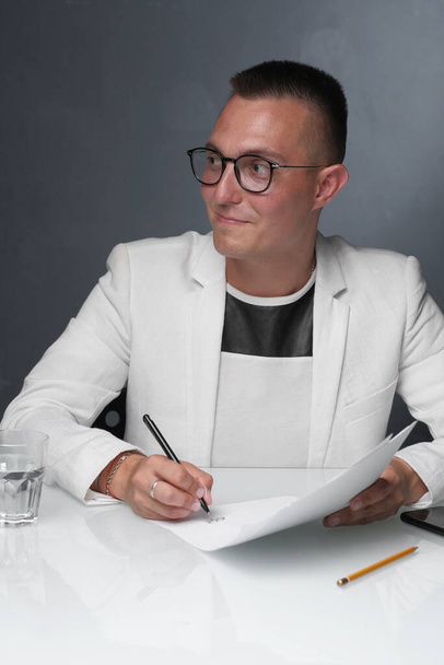 A businessman of 30-35 years old in a white jacket signs important documents. - Φωτογραφία, εικόνα