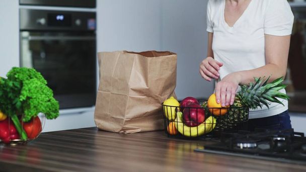 Giovane donna felice porta in cucina una shopping bag con frutta e la disfa. - Foto, immagini