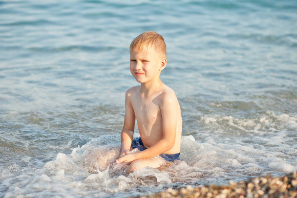 Boy having fun in sea or ocean waves in a summer sunny day. Ocean coast and beach. Active lifestyle and recreation concept. - 写真・画像