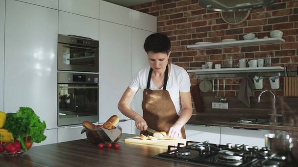 Жінка готує сніданок, обрізаючи багет на дошці на кухні
 - Фото, зображення