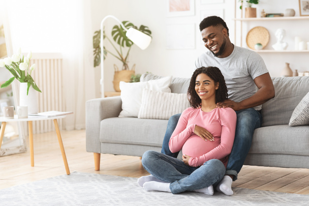 Pregnant black woman enjoying while husband massaging her shoulders - 写真・画像