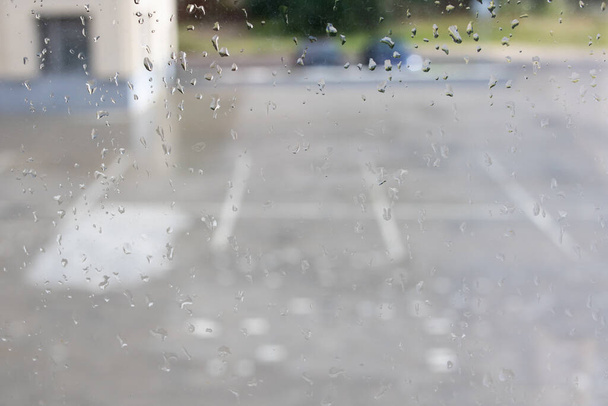 Abstrakter Hintergrund von Regentropfen auf Glas auf dem Hintergrund von Straßen und Stadthäusern - Foto, Bild