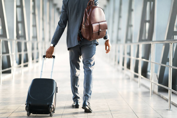 Onherkenbare zakenman die binnenshuis met bagage naar de luchthaven loopt, geknepen - Foto, afbeelding