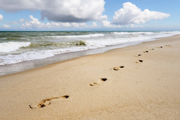 Tło na temat letniego kurortu nadmorskiego. Ślady stóp na piaszczystej plaży nad morzem. Słoneczny krajobraz - Zdjęcie, obraz