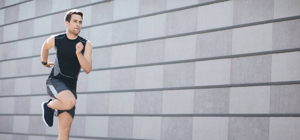 Correr rápido en el entrenamiento en la ciudad. Hombre atlético en ropa deportiva con rastreador de fitness corre y salta
 - Foto, imagen