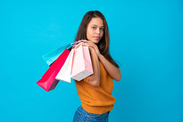 Junge Brasilianerin vor isoliertem blauen Hintergrund mit Einkaufstaschen - Foto, Bild