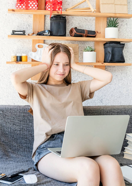 Dálkové studium. Šokovaný teenager dívka studuje pomocí notebooku doma sedí na pohovce drží ruce na hlavě - Fotografie, Obrázek