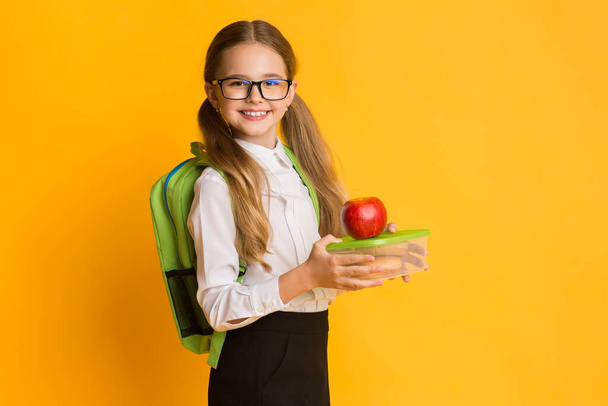 Школа школьница Холдинг школьный обед коробка и красное яблоко, желтый фон - Фото, изображение