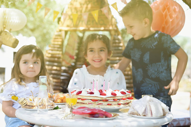 Unkonzentrierter Kinderhintergrund mit Geburtstagstorte im Vordergrund beim Ausblasen der Kerzen. - Foto, Bild