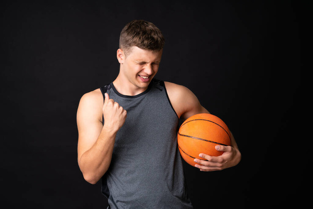 Przystojny młody człowiek gra w koszykówkę nad odizolowaną czarną ścianą - Zdjęcie, obraz