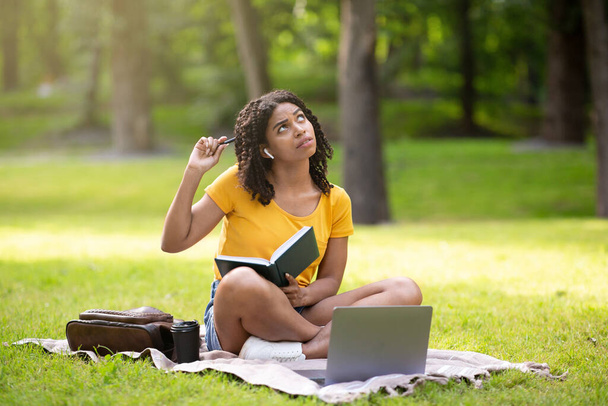Educación a distancia. Chica afroamericana reflexiva haciendo asignación en casa con el ordenador portátil y portátil en el parque
 - Foto, imagen