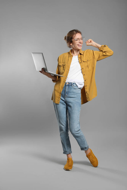 Full length portrait of emotional woman with modern laptop on grey background - Photo, image