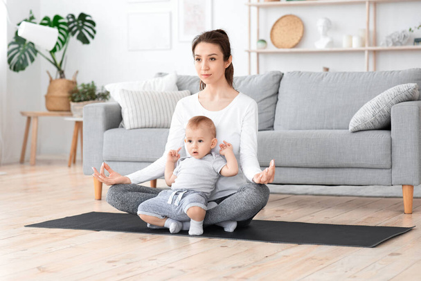 Liberar el estrés en la maternidad. Joven mamá meditando en casa con el bebé en vueltas
 - Foto, Imagen