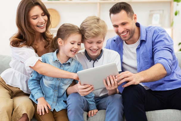 Genitori e bambini che utilizzano tablet seduti sul divano a casa - Foto, immagini