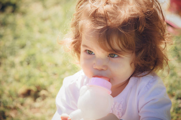 Portrait of a baby girl with a bottle in park - Zdjęcie, obraz