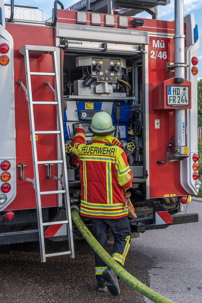 Heidelberg / Baden Wurttemberg - July 22, 2020:  Fireman of German voluntary fire department in front of the open back side of fire truck with water supply connection. Vertical. - Fotografie, Obrázek