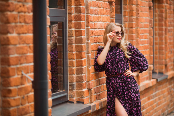 beautiful young female with makeup in a summer dress in sunglasses on a brick wall background - Фото, зображення