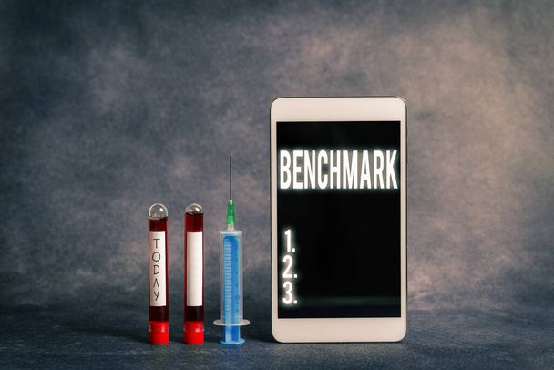 Benchmarkを示すテキスト記号。他の人を測定することができる標準として機能する概念的な写真検査のための準備ができて医療付属品と抽出血液サンプルバイアル. - 写真・画像