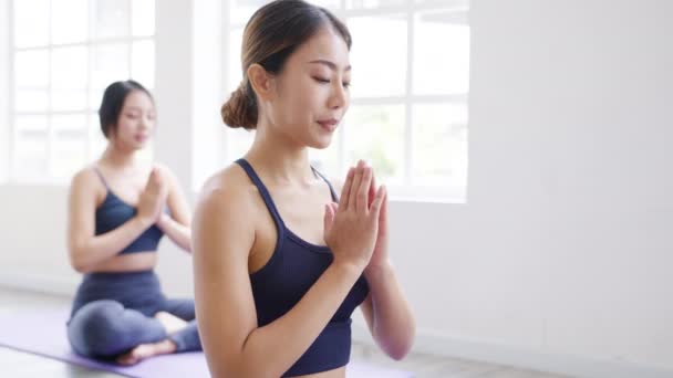 Молодые азиатские спортивные привлекательные люди практикующие йогу с инструктором. Азиатская группа женщин, ведущих здоровый образ жизни в фитнес-студии. Занятия спортом, гимнастикой или балетом. - Кадры, видео