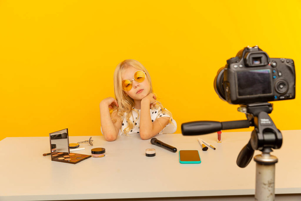 Pequena blogueira no estúdio amarelo na frente da câmera fazendo vídeo. Trabalhando como blogueiro, gravando vídeo tutorial para Internet
. - Foto, Imagem