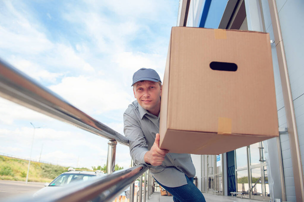 A man in a gray suit in his hands with a cardboard box against the background of the supermarket. Concept on the topic of postal delivery - Foto, immagini