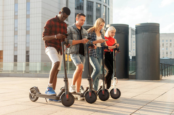 interracial group of young friends rent electric scooters with telephones, multiracial youth connect with smartphones to eco transport, eco transport rental concept - Valokuva, kuva