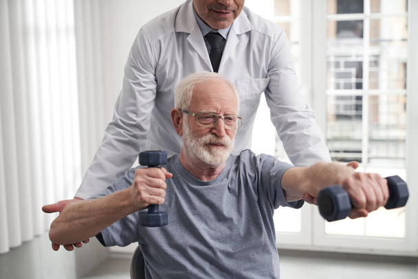 Smiling old man doing upper body workout with rehabilitator - Foto, immagini