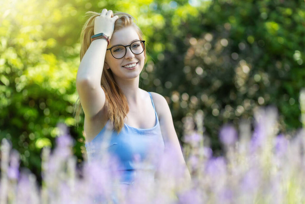 Portrait of smiling young woman posing with glasses behind lavender in the garden - Foto, immagini