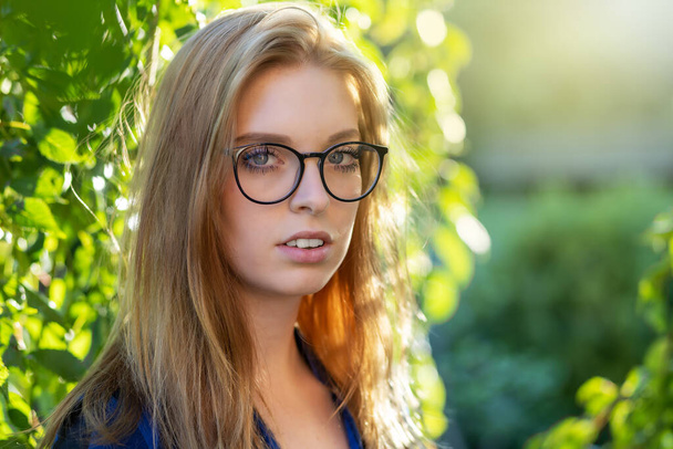 Portrait of young woman posing with glasses in backlight outdoors - 写真・画像