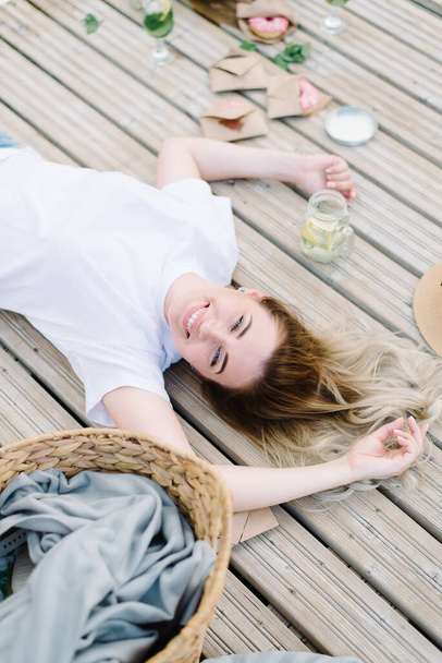 girl in white tshirt lie on a wooden pier. Broad smile, rest, picnic. - Foto, Imagen