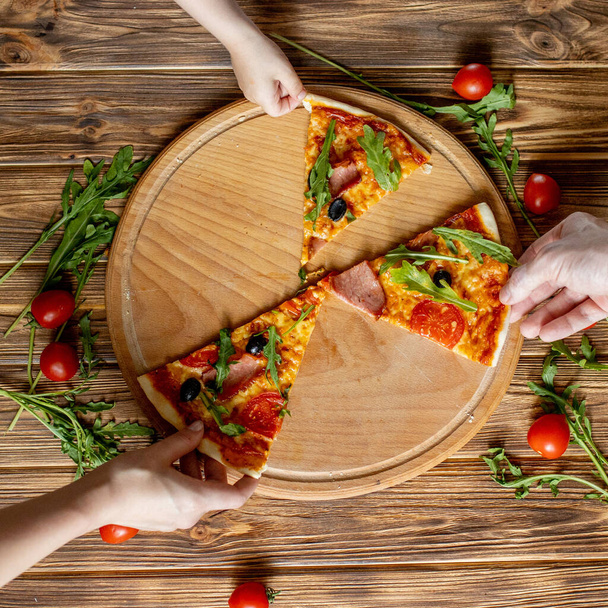 People Hands Taking the last Slices Of Pizza. Pizza and Hands close up over wooden background - Photo, Image