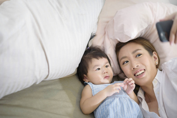 Asian Mother and her baby daughter are making selfie or video call to father in bed , Family , Home safety , parenthood , technology concept . - Foto, Imagem