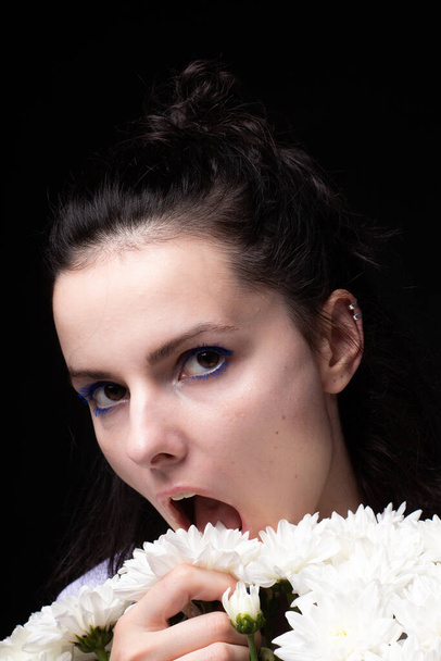 woman eating white chrysanthemums, black background - Foto, imagen