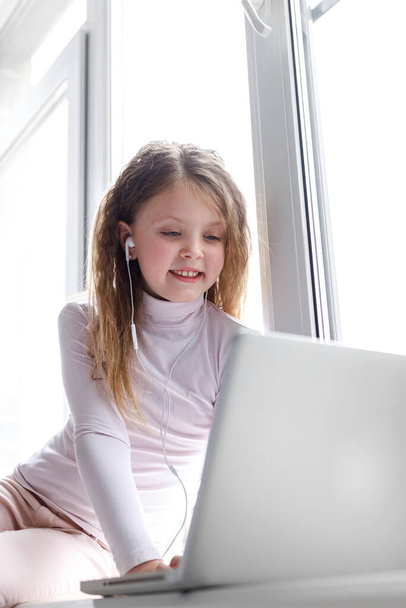 Cute little girl using laptop at home. Vertical photo. The girl at home communicates with friends on the Internet. Education, online study, home studying, schoolgirl children lifestyle concept - Valokuva, kuva