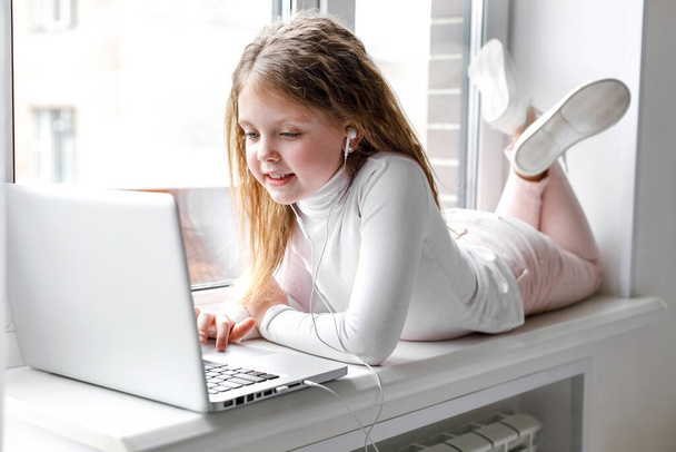 The girl at home communicates with friends on the Internet. Kids distance learning. Cute little girl using laptop at home. Education, online study, home studying, schoolgirl children lifestyle concept - Photo, image