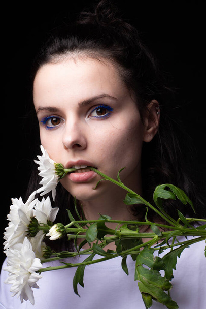 woman with unusual blue makeup holding chrysanthemums in her hands, black studio background - Φωτογραφία, εικόνα