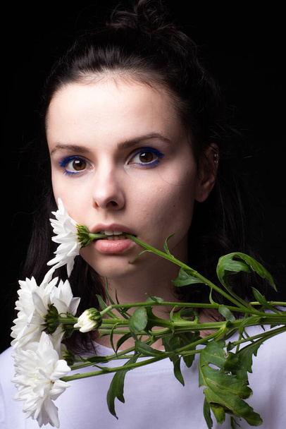Frau mit ungewöhnlich blauem Make-up, Chrysanthemen in den Händen, schwarzer Studiohintergrund - Foto, Bild