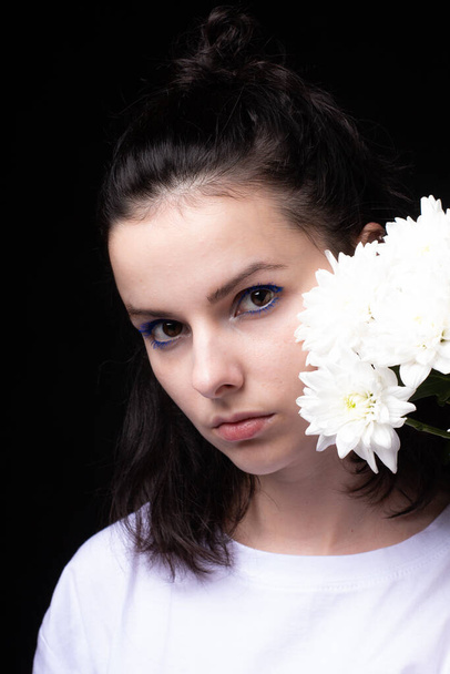 woman with unusual blue makeup holding chrysanthemums in her hands, black studio background - Foto, afbeelding