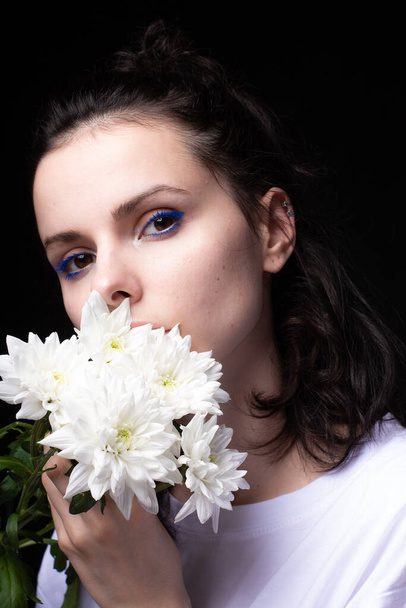 woman with unusual blue makeup holding chrysanthemums in her hands, black studio background - Foto, Imagen