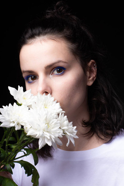 woman with unusual blue makeup holding chrysanthemums in her hands, black studio background - Фото, зображення