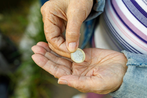 Κέρμα στο χέρι της γριάς κυρίας. Μια ηλικιωμένη γυναίκα με ένα ευρώ στα χέρια της. Κοντινό πλάνο - Φωτογραφία, εικόνα