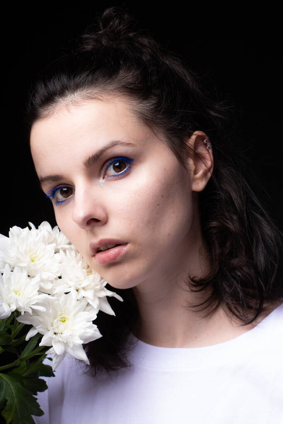 woman with unusual blue makeup holding chrysanthemums in her hands, black studio background - Foto, imagen