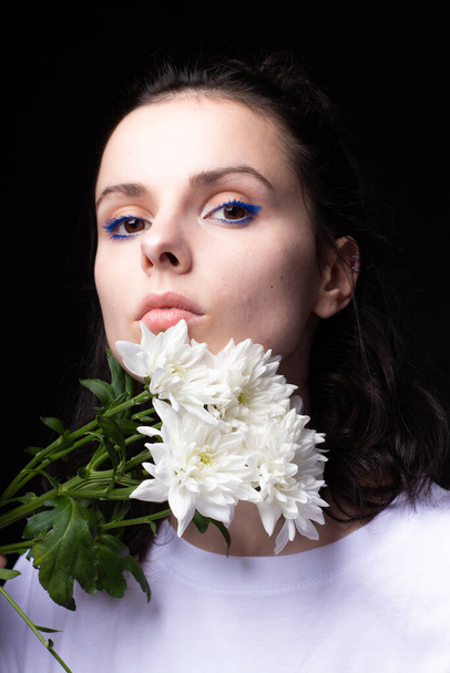 woman with unusual blue makeup holding chrysanthemums in her hands, black studio background - Photo, Image