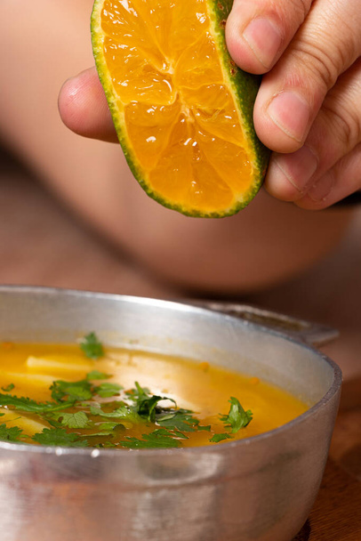 Mano de persona exprimiendo un limon en una sopa de papa con cilantro y perejil. Plato de comida tradicional colombiana - Фото, изображение